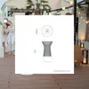 A couple is standing on a wooden deck at night, with string lights overhead. A diagram of a table with dimensions is overlaid on the image. Produktbild-Vorschau