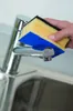 A hand is cleaning a kitchen faucet with a sponge. Podgląd zdjęcia produktu