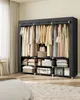 A portable fabric wardrobe is shown in a room, filled with clothes and storage boxes. A portion of a bed is visible in the foreground, and a window with curtains is in the background. Náhled obrázku produktu