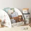 A children's bookshelf organizer filled with books and a teddy bear, next to a stack of decorative storage boxes. Produktbild-Vorschau