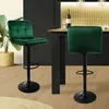 Two green velvet bar stools are shown in a modern kitchen setting, with a bottle of wine and glasses on the counter. Podgląd zdjęcia produktu