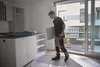A man is carrying a flat panel in a room that appears to be under renovation, with kitchen cabinets and shelves visible. Voir les images du produit