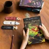 A pair of hands holding a Harry Potter book, with several Harry Potter themed bookmarks laid out on a wooden table. Produktbild-Vorschau