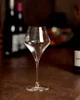 A clear wine glass is placed on a brown countertop, with blurred bottles in the background. Produktbild-Vorschau