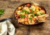 A close-up shot of a pan filled with grilled cheese, tomatoes, and basil, served on a wooden table. Produktbild-Vorschau