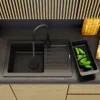 A black kitchen sink with a faucet and a basket of cucumbers next to it. Podgląd zdjęcia produktu