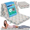 A woman is lying on a folded mattress, with a folded mattress and a box of the same mattress shown in the background. The mattress has a rainbow pattern. Produktbild-Vorschau