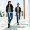 Two young people wearing helmets riding Razor scooters outdoors. Produktbild-Vorschau