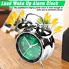 A close-up shot of a retro alarm clock with a green face, placed on a wooden surface. Yellow lightning bolt graphics are overlaid on the image, suggesting loudness. Voir les images du produit
