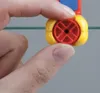 A close-up shot of a person's fingers holding a small yellow and red component, possibly a part of a tool or toy. Produktbild-Vorschau