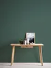 A wooden desk with a framed picture, a plant, and decorative items against a dark green wall. Produktbild-Vorschau