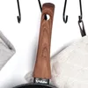 A close-up view of a frying pan handle with a wooden grip, hanging on hooks next to kitchen towels. Produktbild-Vorschau