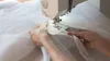A close-up shot of a person's hands sewing a white sheer fabric on a sewing machine. Produktbild-Vorschau