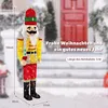 A large illuminated nutcracker figure stands in front of a snowy doorway, with text overlays indicating Christmas greetings and product specifications. Produktbild-Vorschau