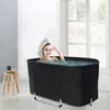 A woman with a towel on her head and a face mask is relaxing in a black portable bathtub filled with water. Náhled obrázku produktu