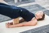 A woman is doing yoga on a mat outdoors, supported by a yoga block. Produktbild-Vorschau