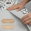 Hands are shown ironing a piece of grey fabric on a patterned surface, with a roll of tape and scissors visible. Náhled obrázku produktu