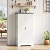A white cabinet with a dark top is shown in a room with wooden floors and white paneled walls. A window with a view of a garden is visible to the left. A plant in a woven pot sits to the right. Anteprima dell’immagine prodotto