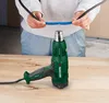 A person is holding two wires, one blue and one black, in front of a green Parkside heat gun on a wooden surface. Produktbild-Vorschau