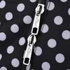 A close-up shot of two zippers on a black and white polka-dot fabric. Produktbild-Vorschau
