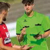 A soccer referee in a bright green uniform is talking to a player in a red uniform on a soccer field. Anteprima dell’immagine prodotto