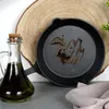 A cast iron pan with oil in it, next to a bottle of olive oil, on a wooden board. Produktbild-Vorschau
