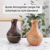 Two diffusers with wood grain texture are displayed on a speckled surface with a blurred background of greenery and furniture. Produktbild-Vorschau
