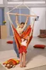 Two children are enjoying a colorful hammock chair indoors, with pillows scattered on the floor. Produktbild-Vorschau