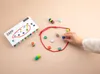A person's hand is placing a blue token into a red loop on a light beige surface, next to a game box. Voir les images du produit