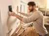 A man is using a Bosch digital stud finder on a wall in a kitchen. Voir les images du produit