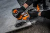 A person wearing black gloves is using a cordless angle grinder to cut a piece of stone or tile. Dust is visible in the air. Voir les images du produit