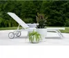 A white lounge chair with two potted plants on a patio. Produktbild-Vorschau