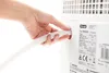 A hand connects a ribbed white hose to the back of a white appliance. A label with text and a De'Longhi logo is visible on the appliance. Voir les images du produit