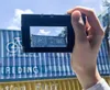 A hand holding a digital camera, taking a picture of a shipping container with a bicycle logo and text. Náhľad obrázku produktu