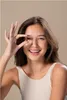 A young woman is holding a capsule between her fingers and smiling. Produktbild-Vorschau