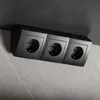 A black triple power strip is mounted on a wall with a marble pattern. Náhled obrázku produktu