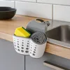 A kitchen sink organizer with a sponge and steel wool is placed on a countertop next to a sink. Podgląd zdjęcia produktu