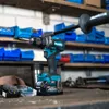 A cordless drill is shown on a workbench in a workshop setting, with shelves of blue storage bins in the background. Anteprima dell’immagine prodotto