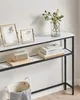 A narrow console table with marble-effect top and two shelves, decorated with picture frames, a vase with flowers, books, and a small speaker. Náhled obrázku produktu