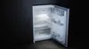 An open refrigerator with its interior light on, against a dark background. Produktbild-Vorschau