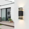 A black outdoor wall light with clear glass accents is mounted on a white wall next to a modern house with a wooden deck and sliding glass doors. Produktbild-Vorschau