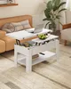 A white lift-top coffee table is shown in a living room setting, with a laptop, fruit, and books on it. Voir les images du produit