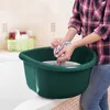 A person is washing a colorful cloth in a green basin in a bathroom. Anteprima dell’immagine prodotto