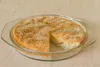 A round glass baking dish with a pie or cake topped with sesame seeds, with one slice removed. Produktbild-Vorschau