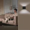 A man and his dog relaxing on a couch in a living room, with a wall-mounted light fixture illuminating the wall. Podgląd zdjęcia produktu