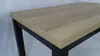 A close-up view of a table with a wood-grain surface and black legs. Náhled obrázku produktu