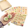 A hand holding wooden memory game pieces with leaves on them, with the game board and cards in the background. Anteprima dell’immagine prodotto