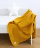 A mustard yellow muslin blanket draped over the side of a white crib. Produktbild-Vorschau