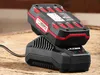 A black and red battery charger with a battery pack on top, resting on a wooden surface. Produktbild-Vorschau