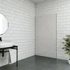 A modern bathroom with white subway tiles on the walls and a large, textured gray panel on the right wall. A white sink is mounted on a dark metal stand with a gray towel hanging from it. The floor is dark gray. Produktbild-Vorschau